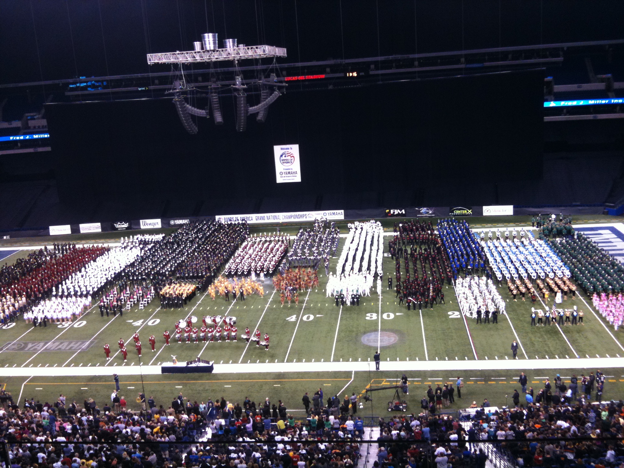High school marching bands performing on a football field at night.