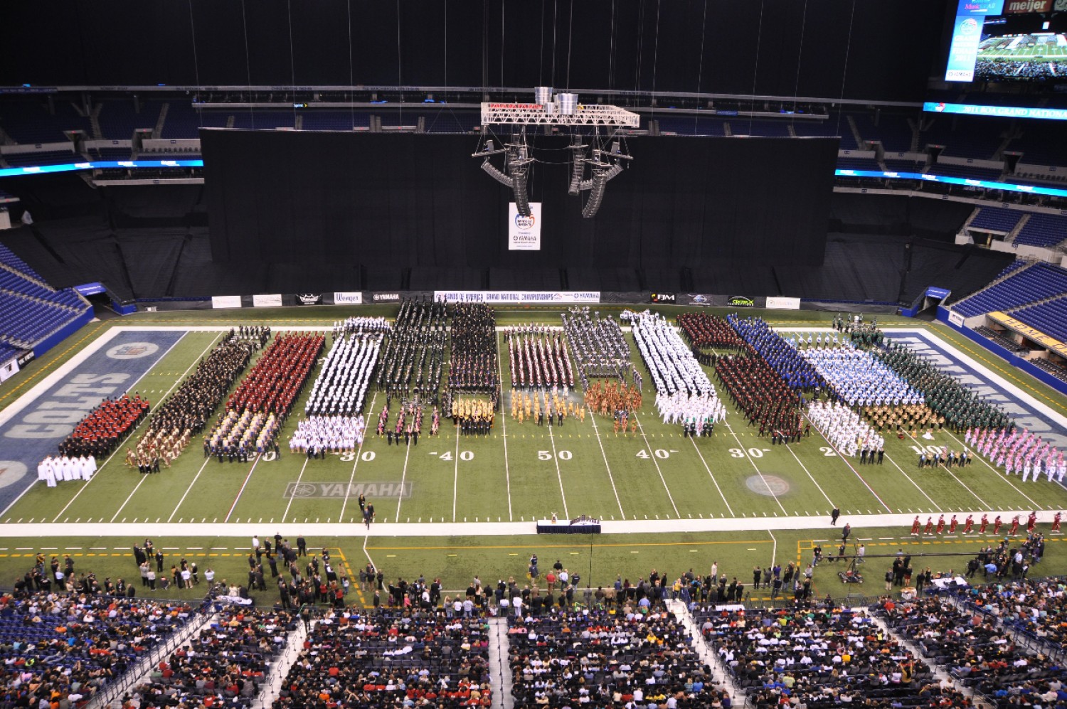 Large marching bands perform on a football field with an audience watching.