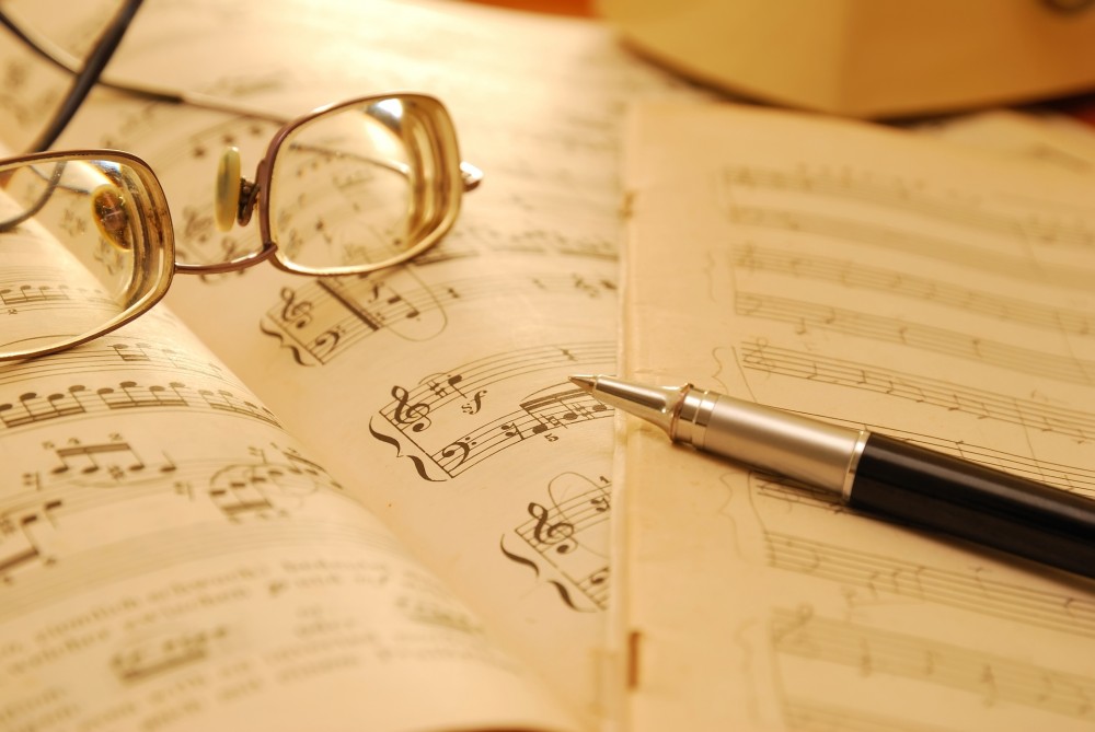 Pen and glasses rest on scattered sheet music pages.