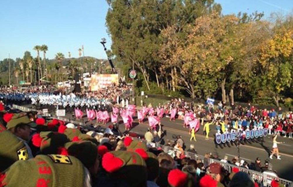 A parade with dancers in pink and white costumes performing on a sunny day.