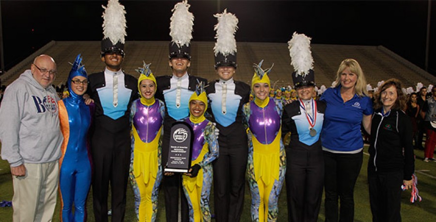 A group of performers in colorful costumes posing with a trophy.