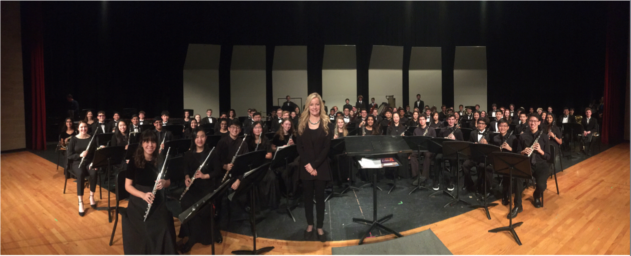 A woman stands in front of a large orchestra on stage.